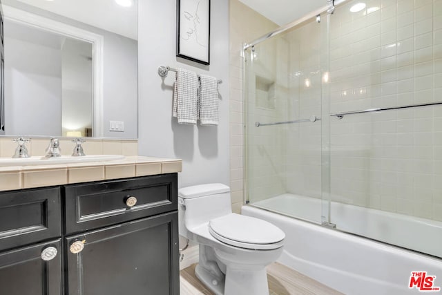 full bathroom featuring hardwood / wood-style floors, vanity, toilet, and shower / bath combination with glass door