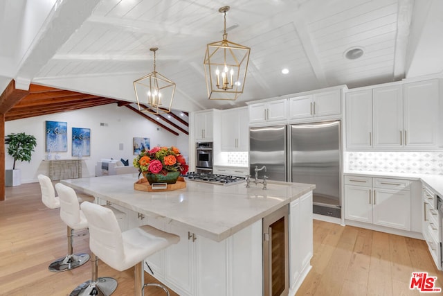 kitchen featuring appliances with stainless steel finishes, pendant lighting, light hardwood / wood-style flooring, white cabinets, and vaulted ceiling with beams