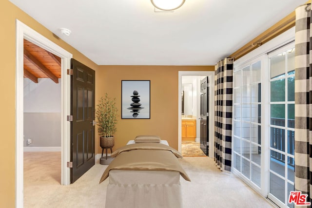 bedroom featuring ensuite bath, light colored carpet, and vaulted ceiling with beams