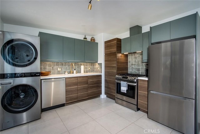 kitchen featuring sink, tasteful backsplash, stacked washer and dryer, light tile patterned floors, and appliances with stainless steel finishes