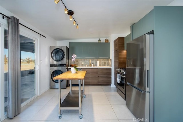 kitchen featuring stacked washer and dryer, green cabinetry, light tile patterned floors, tasteful backsplash, and stainless steel appliances