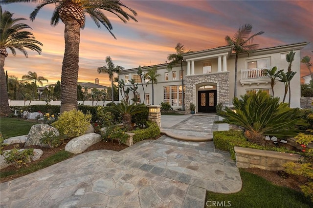 view of front facade featuring a balcony, stucco siding, stone siding, and french doors