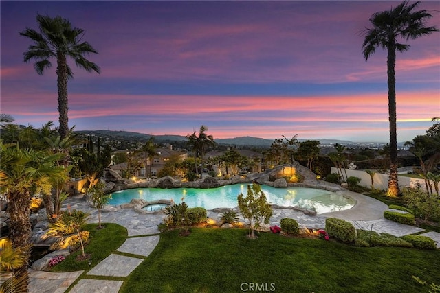 pool at dusk with fence, an outdoor pool, a lawn, and an in ground hot tub