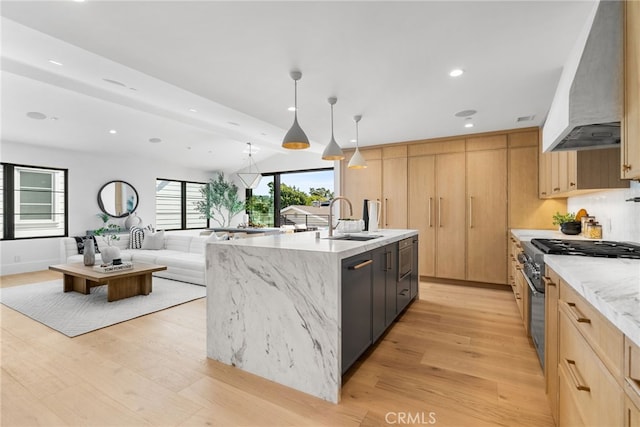 kitchen with stainless steel stove, decorative light fixtures, an island with sink, sink, and custom range hood