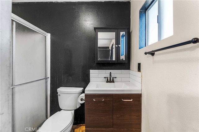 bathroom featuring a shower with door, vanity, backsplash, and toilet