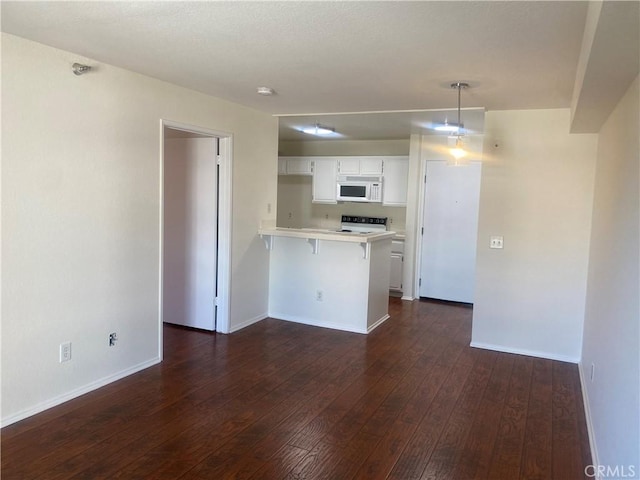 kitchen featuring dark wood-type flooring, a kitchen breakfast bar, kitchen peninsula, white appliances, and white cabinets