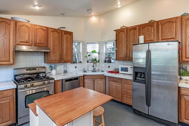 kitchen with appliances with stainless steel finishes, lofted ceiling, a kitchen island, sink, and backsplash