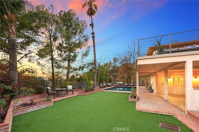 yard at dusk featuring a fenced in pool, a patio area, and a balcony