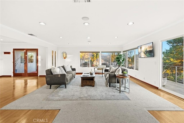 living room featuring a wealth of natural light, ornamental molding, and light wood-type flooring