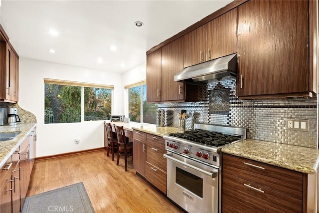 kitchen featuring light stone countertops, decorative backsplash, premium stove, and light hardwood / wood-style floors