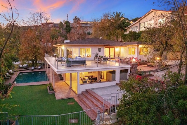 back house at dusk featuring a fenced in pool, a balcony, and a patio