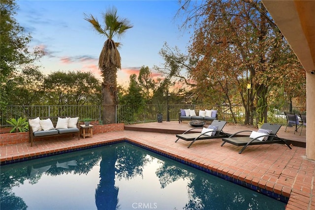 pool at dusk featuring a patio area and an outdoor living space