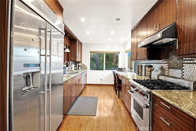 kitchen featuring high end appliances, light stone countertops, sink, tasteful backsplash, and light wood-type flooring