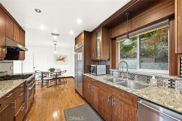 kitchen featuring light wood-type flooring, premium appliances, hanging light fixtures, and sink