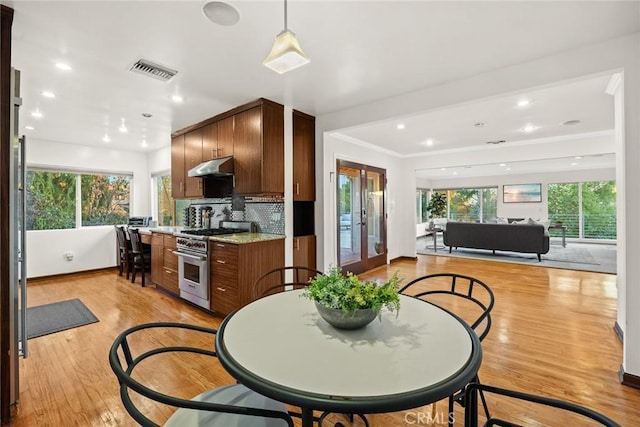 kitchen with light stone countertops, decorative backsplash, high end stove, crown molding, and light hardwood / wood-style flooring