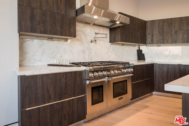 kitchen featuring light hardwood / wood-style flooring, range with two ovens, tasteful backsplash, and wall chimney exhaust hood