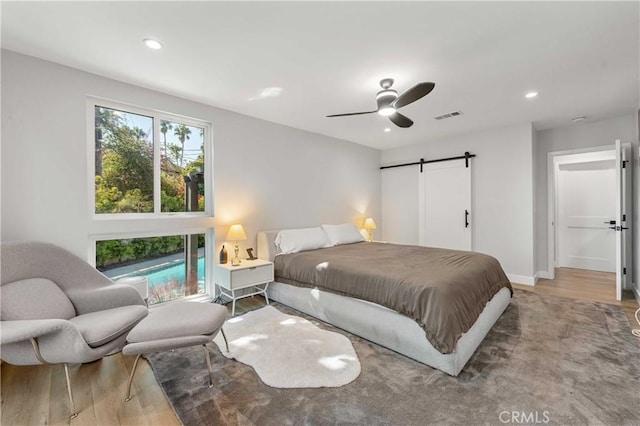 bedroom with a barn door, ceiling fan, and light hardwood / wood-style flooring