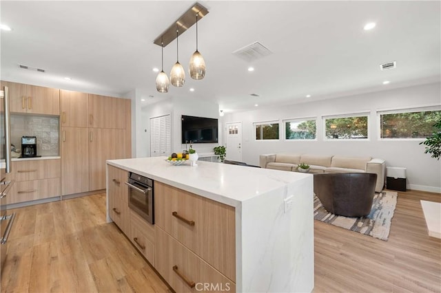 kitchen with pendant lighting, oven, light wood-type flooring, light brown cabinetry, and a kitchen island