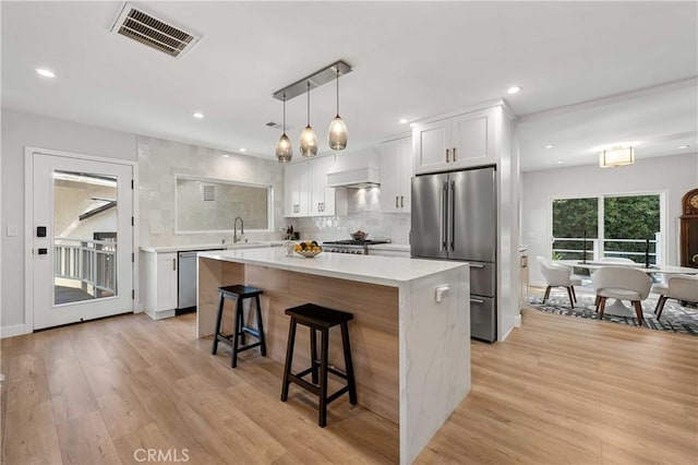 kitchen with white cabinetry, light hardwood / wood-style flooring, a kitchen island, custom range hood, and stainless steel appliances