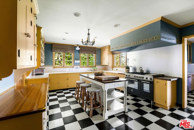 kitchen with a kitchen island, wall chimney exhaust hood, wooden counters, an inviting chandelier, and double oven range