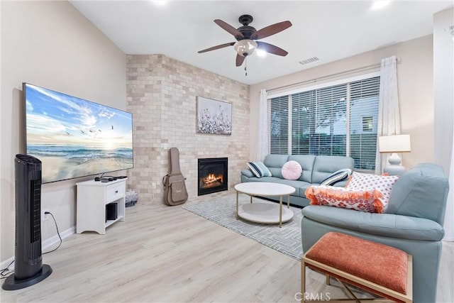 living room with ceiling fan, a large fireplace, and light hardwood / wood-style flooring