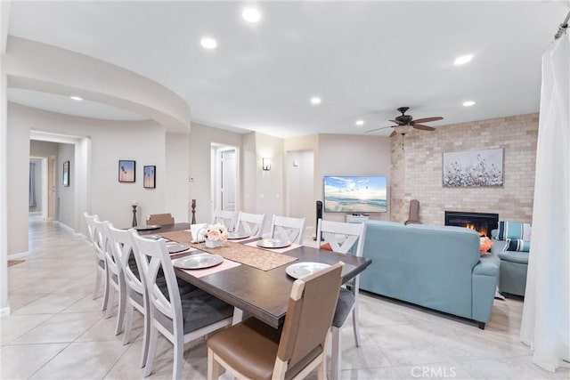 tiled dining space with a large fireplace and ceiling fan