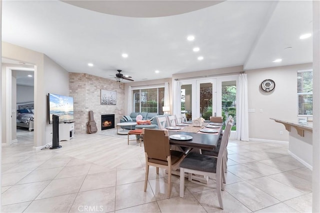 dining space with light tile patterned floors, a large fireplace, and ceiling fan