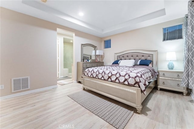 bedroom featuring a raised ceiling, connected bathroom, and light hardwood / wood-style flooring