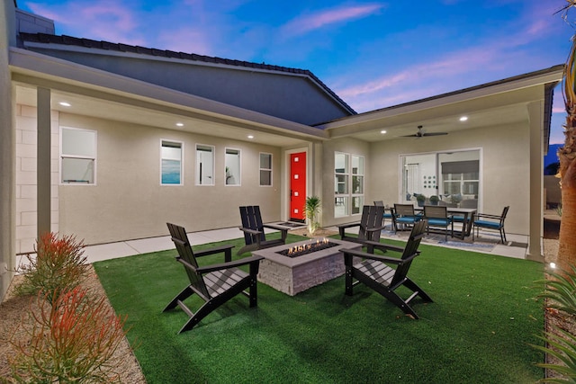 back house at dusk with a patio, ceiling fan, an outdoor living space with a fire pit, and a yard