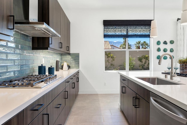 kitchen featuring wall chimney range hood, hanging light fixtures, stainless steel appliances, backsplash, and sink