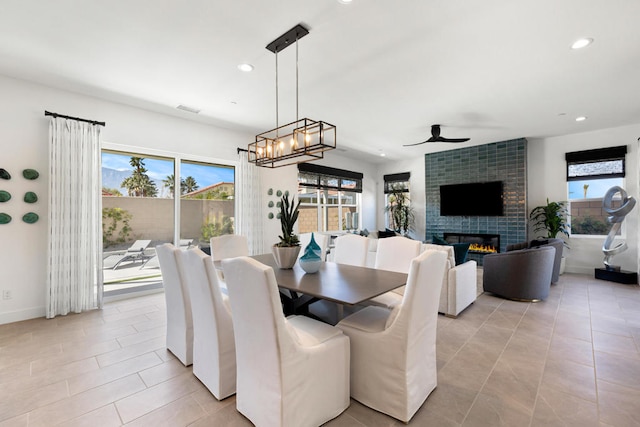 tiled dining space with a tiled fireplace, a wealth of natural light, and ceiling fan with notable chandelier