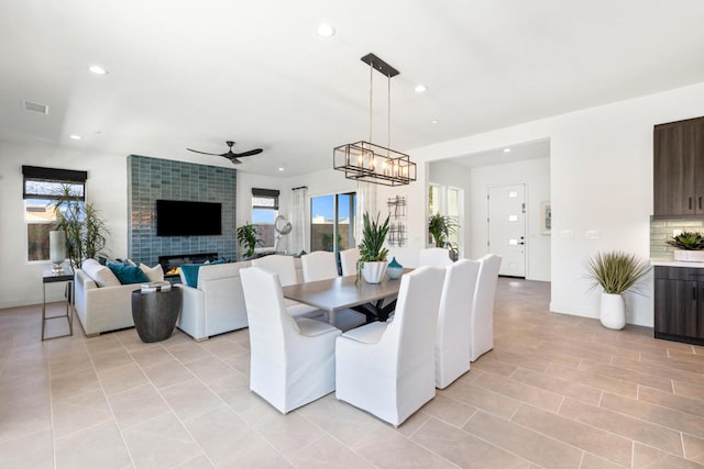 dining area with light tile patterned flooring, ceiling fan with notable chandelier, and a tile fireplace