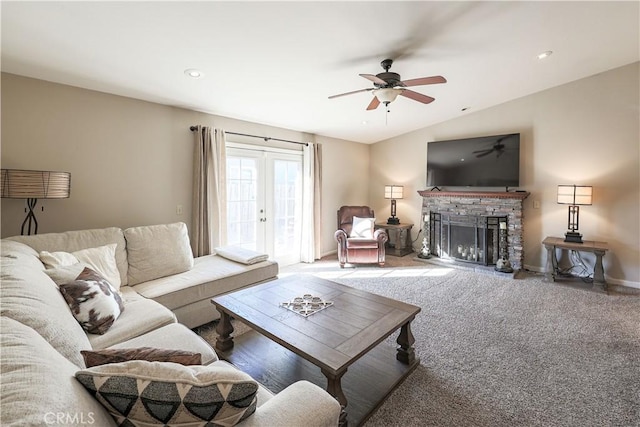 carpeted living room with french doors, a stone fireplace, ceiling fan, and lofted ceiling