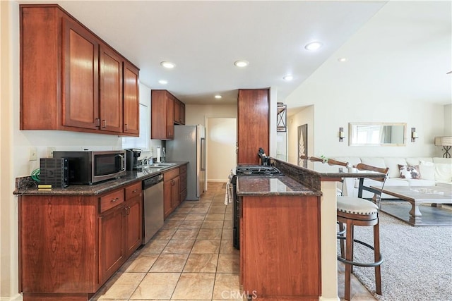 kitchen featuring stainless steel appliances, kitchen peninsula, dark stone counters, a kitchen bar, and light tile patterned flooring