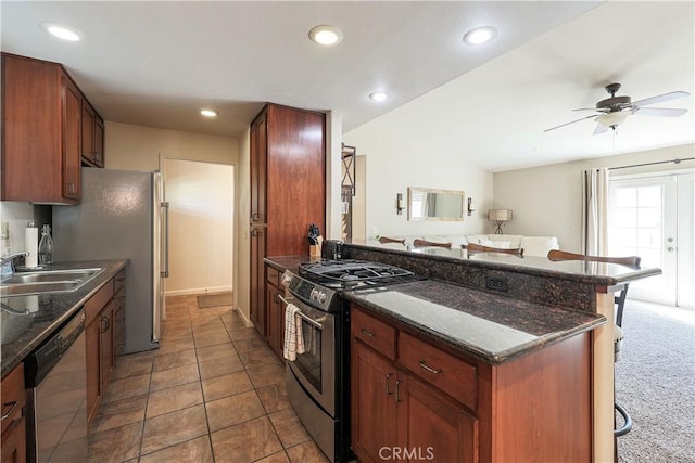 kitchen featuring dark stone counters, sink, ceiling fan, appliances with stainless steel finishes, and a breakfast bar area