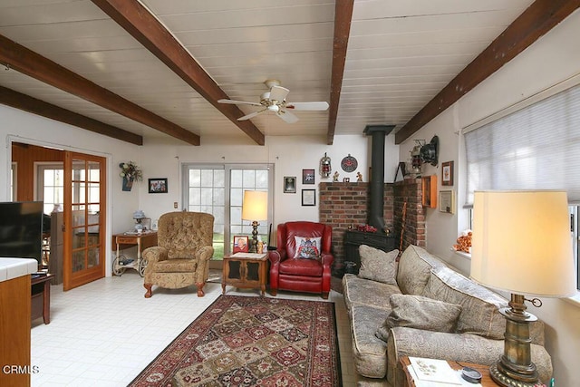 living room featuring a wood stove, ceiling fan, beamed ceiling, and wooden ceiling