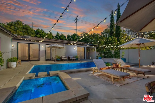 pool at dusk with an in ground hot tub and a patio area