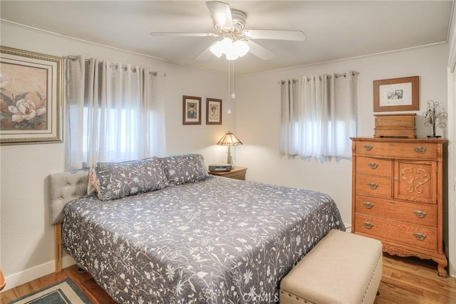 bedroom featuring multiple windows, hardwood / wood-style floors, ornamental molding, and ceiling fan