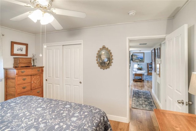 bedroom with hardwood / wood-style flooring, ceiling fan, crown molding, and a closet