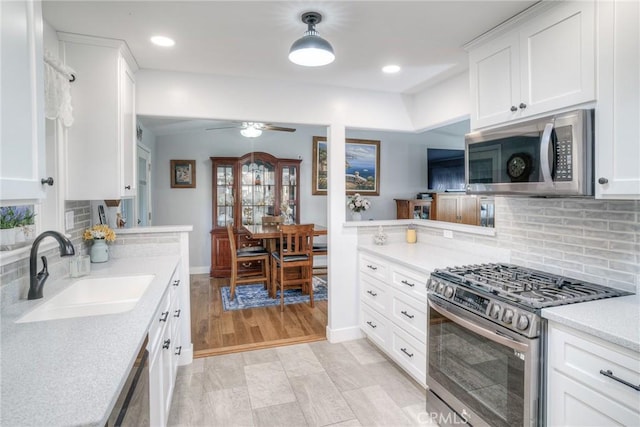 kitchen with sink, kitchen peninsula, pendant lighting, stainless steel appliances, and white cabinets