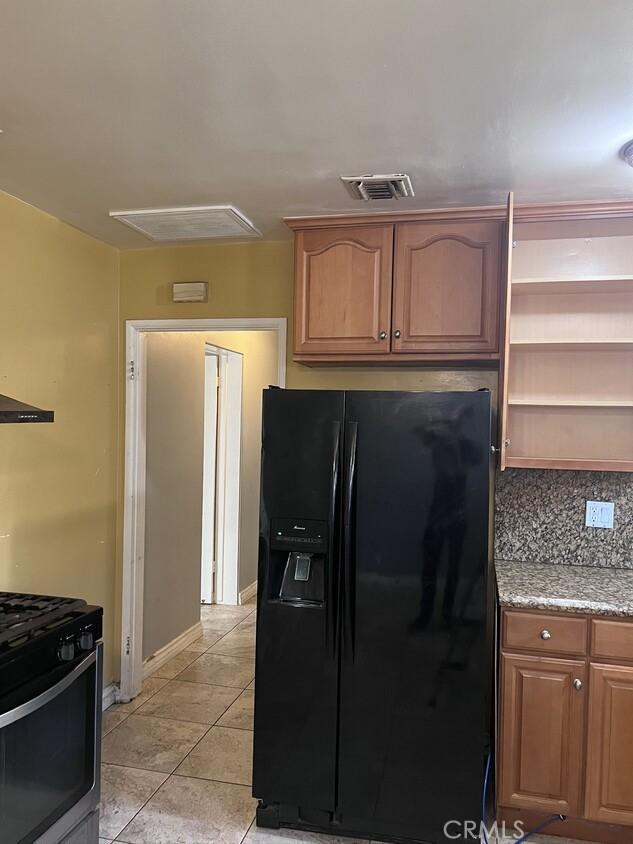 kitchen with light stone countertops, decorative backsplash, black fridge with ice dispenser, light tile patterned floors, and stainless steel range with gas stovetop