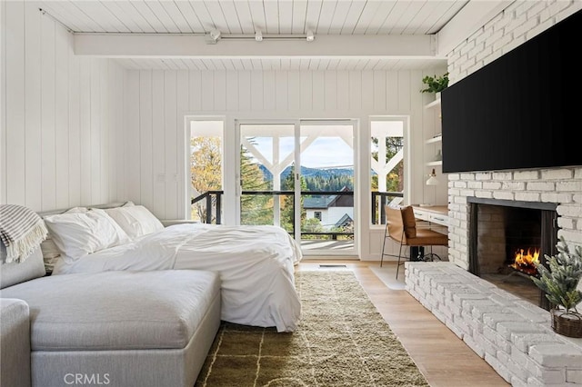 bedroom featuring a fireplace, hardwood / wood-style flooring, access to outside, track lighting, and beam ceiling