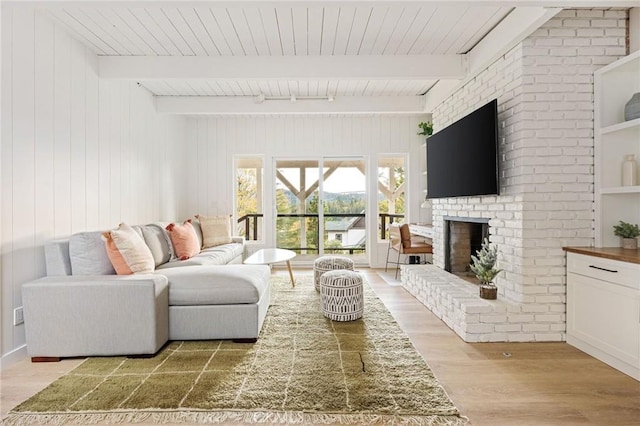 living room featuring beamed ceiling, wooden walls, a fireplace, and light hardwood / wood-style flooring