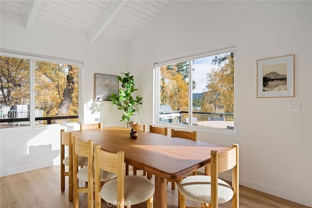 dining area with a healthy amount of sunlight, light hardwood / wood-style floors, and vaulted ceiling with beams