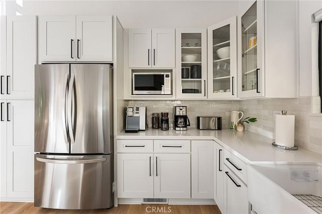 kitchen featuring built in microwave, white cabinetry, tasteful backsplash, stainless steel refrigerator, and light hardwood / wood-style floors