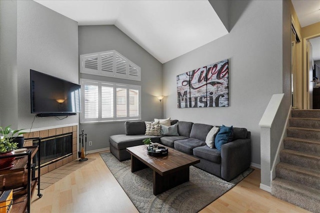 living room with a tile fireplace, lofted ceiling, and light wood-type flooring