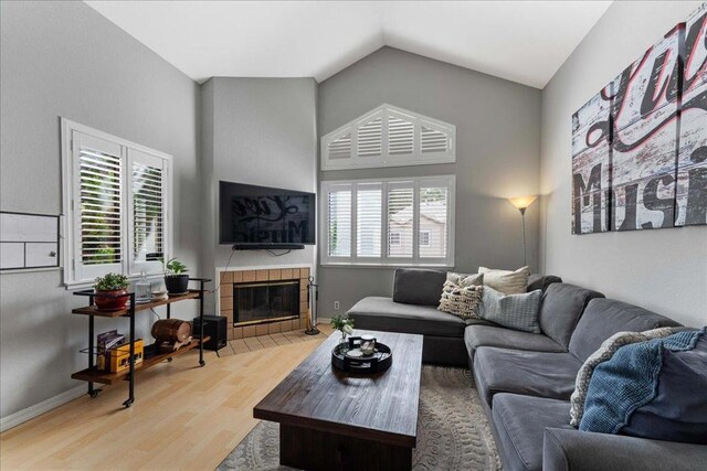 living room with hardwood / wood-style floors, vaulted ceiling, a tiled fireplace, and a healthy amount of sunlight