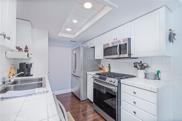 kitchen featuring appliances with stainless steel finishes, sink, tile countertops, white cabinets, and dark wood-type flooring