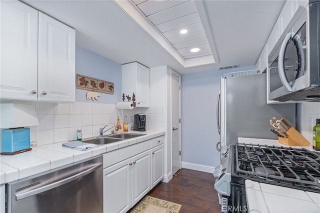 kitchen with appliances with stainless steel finishes, tile countertops, white cabinetry, and dark hardwood / wood-style flooring