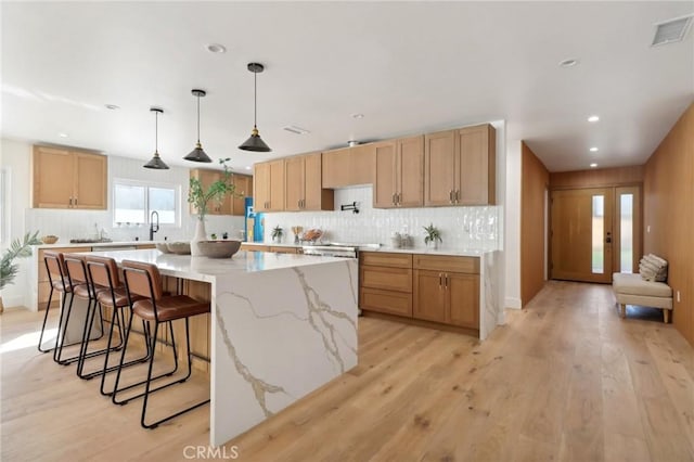 kitchen with light stone countertops, a large island, sink, hanging light fixtures, and light hardwood / wood-style flooring